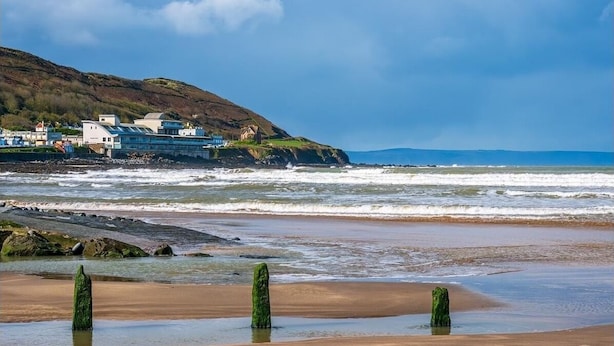 Un paysage côtier avec des bâtiments situés sur une falaise, une plage de sable et des vagues qui déferlent sur le rivage.