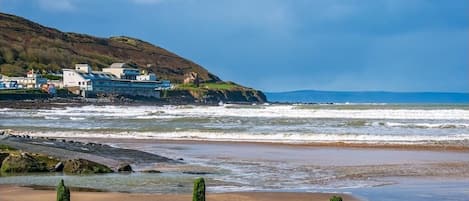 Un paysage côtier avec des bâtiments situés sur une falaise, une plage de sable et des vagues qui déferlent sur le rivage.