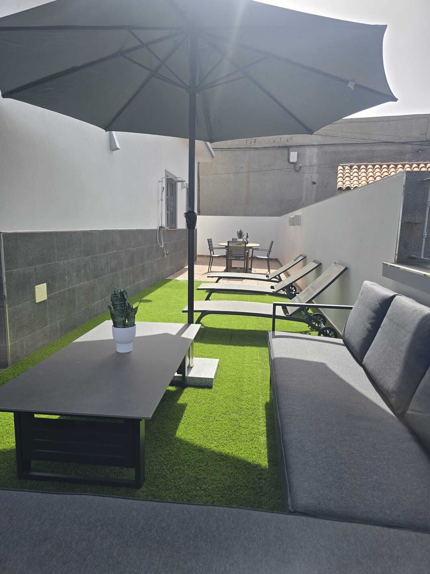 Een patio met een tafel, stoelen, een bank en een parasol.