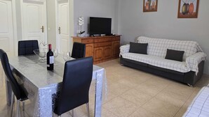 A living room with a dining table, chairs, a sofa, a TV, and a cabinet.