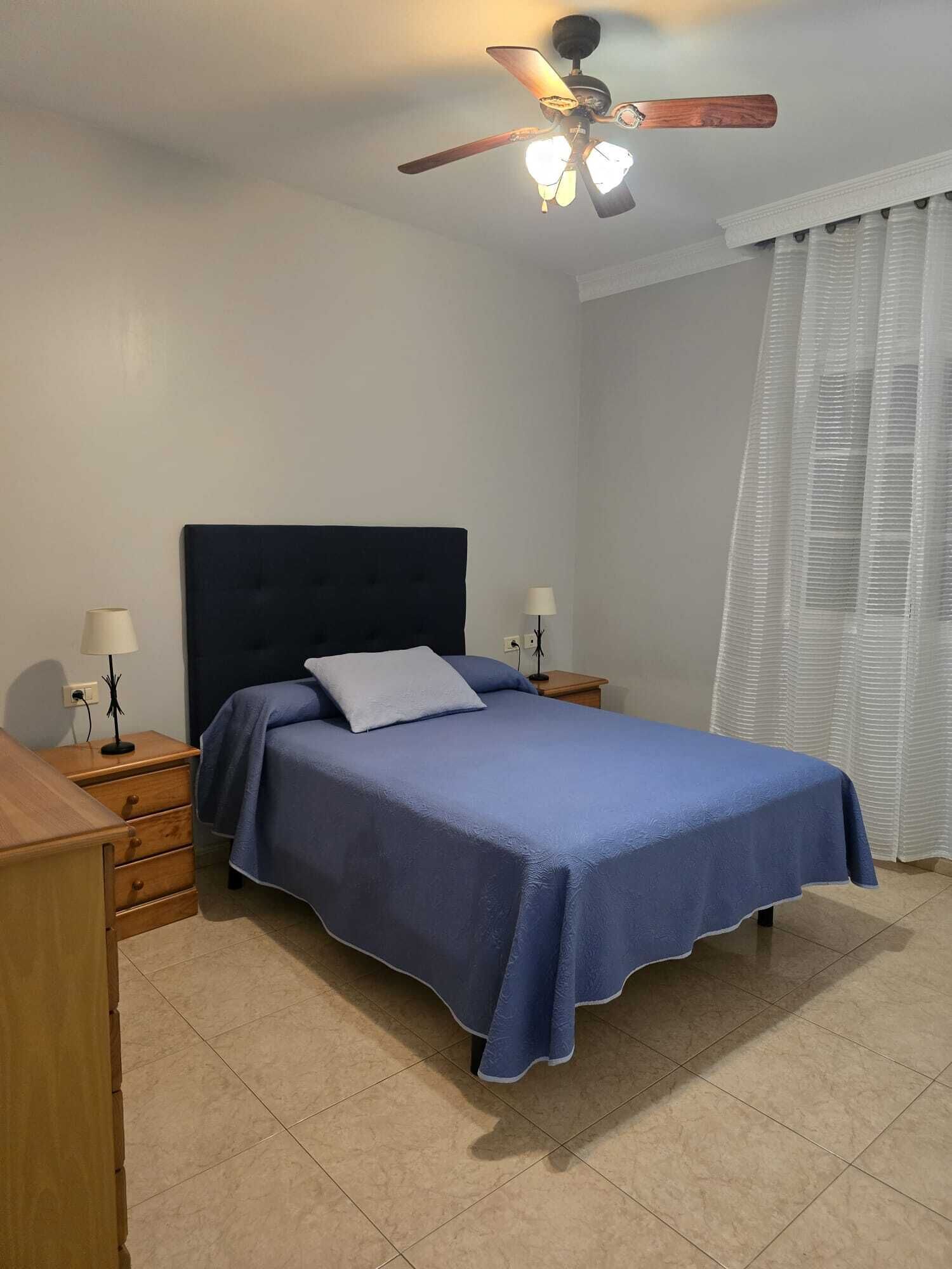 Ein Schlafzimmer mit einem Bett, zwei Nachttischen, einem Deckenventilator und einem Fenster mit Vorhängen.