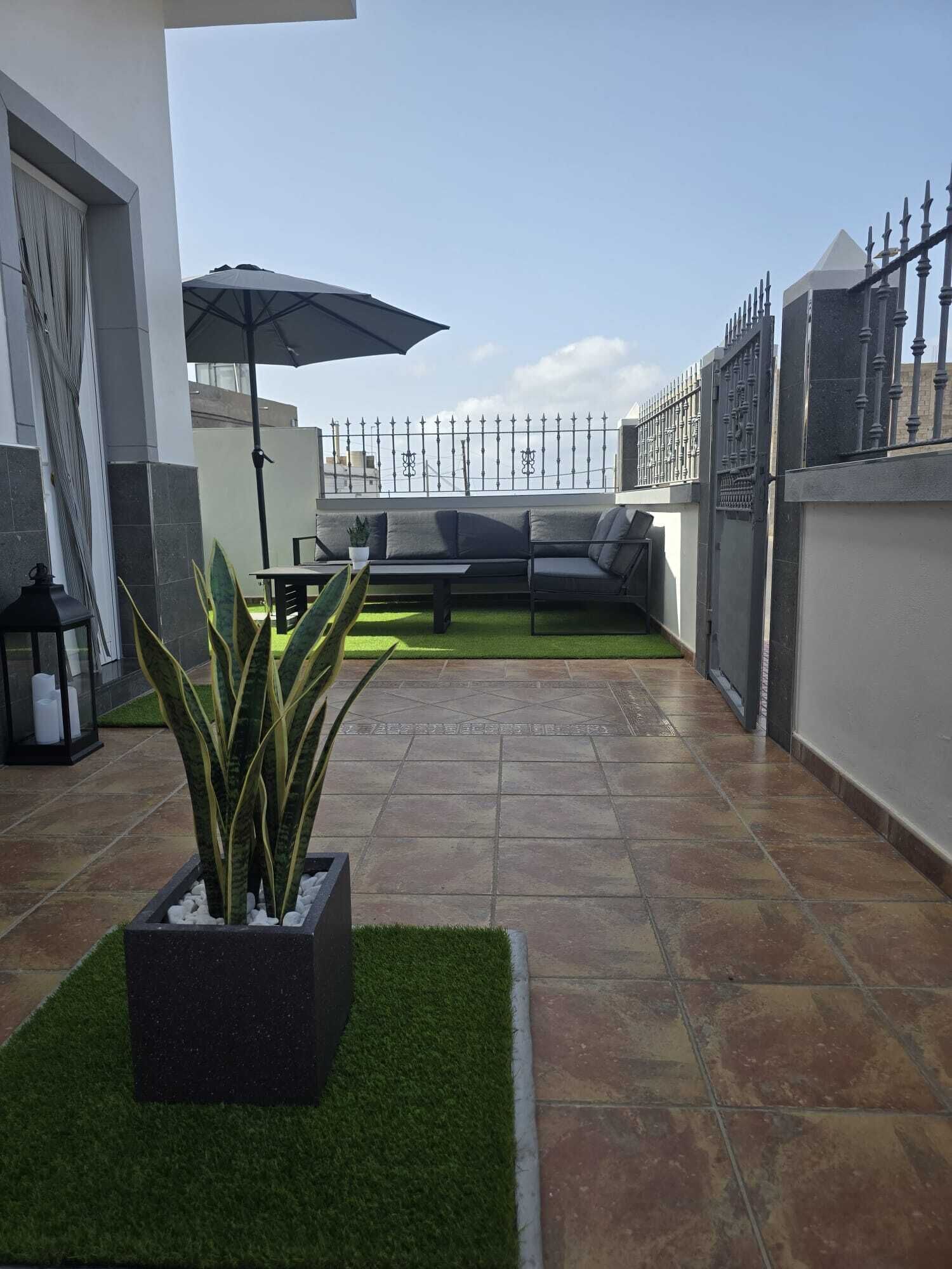 Une terrasse sur le toit, avec un espace salon, un pot de fleurs et une clôture décorative.