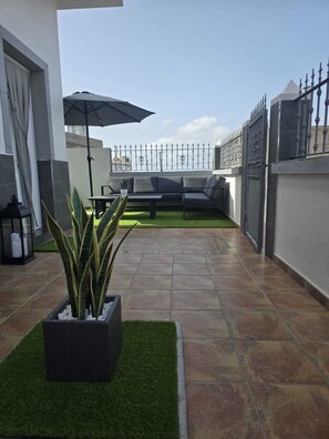 A rooftop patio with a seating area, a potted plant, and a decorative fence.
