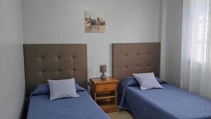 A room with two beds, a nightstand, a lamp, a painting on the wall, and a window with curtains.