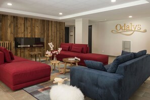 A modern living room with red and blue sofas, a wooden accent wall, a flat-screen TV, and a decorative sign. - Apartment in Chamonix with Heated Pool (Chamonix mont blanc)