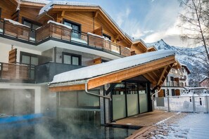A modern chalet with a wooden exterior, a covered outdoor pool, and a view of snow-capped mountains. - Apartment in Chamonix with Heated Pool (Chamonix mont blanc)