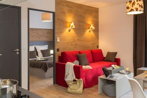 A modern hotel room with a red sofa, a desk with a laptop, and a wooden accent wall. - Apartment in Chamonix with Heated Pool (Chamonix mont blanc)