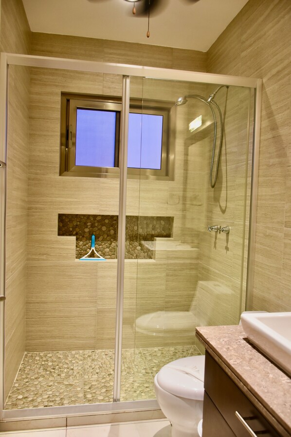 A modern bathroom with a glass-enclosed shower, a toilet, and a sink with a marble countertop.