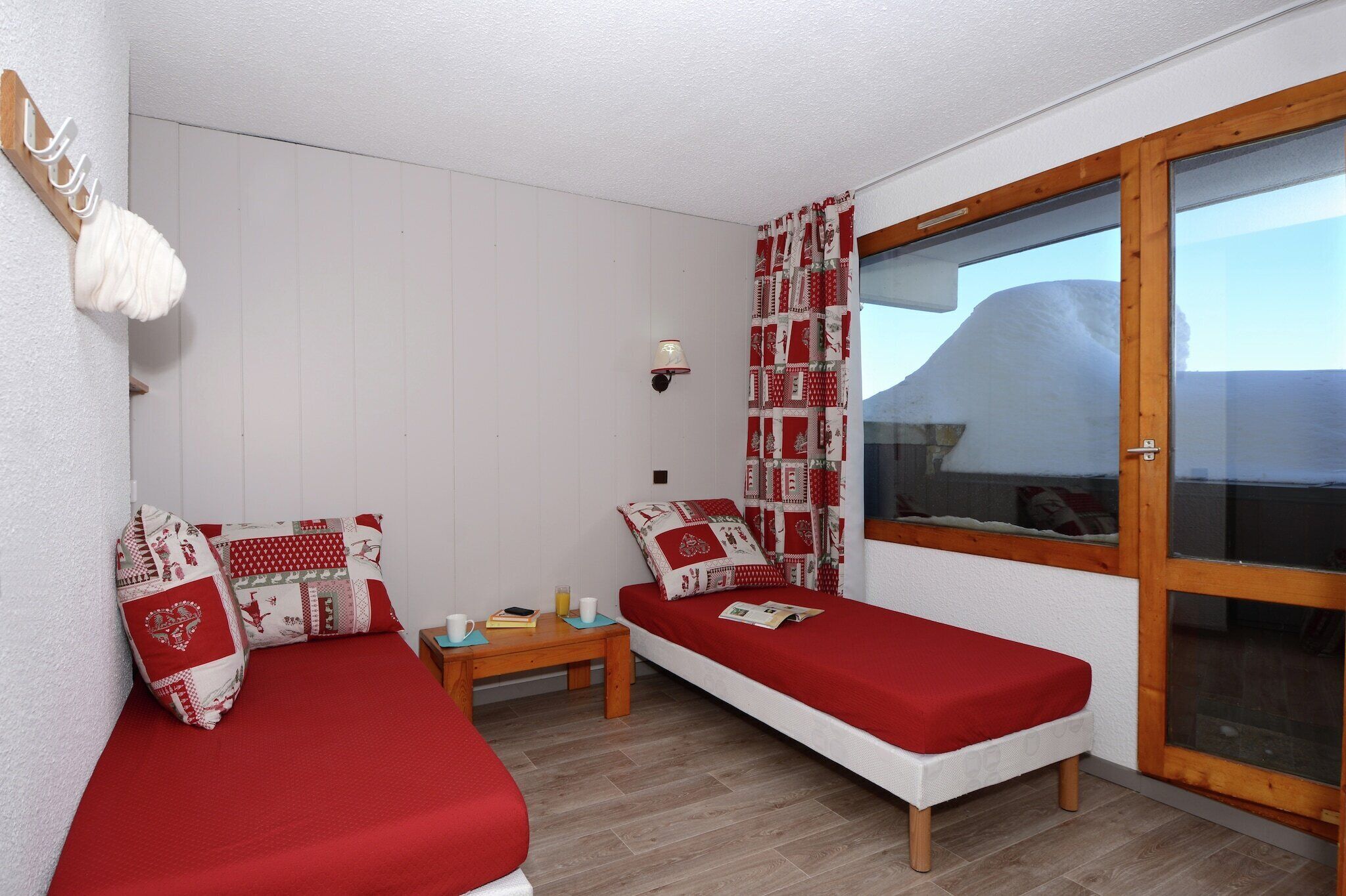 Une chambre avec deux lits simples, une petite table, une lampe fixée au mur et une fenêtre donnant sur des collines enneigées.
