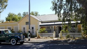 A vintage green car parked in front of a yellow building with a white picket fence and a white gazebo. - Saxe-Coburg Lodge (Prince Albert)