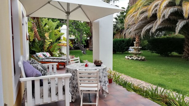 An outdoor patio with a table and chairs, surrounded by lush greenery and a small fountain. - Saxe-Coburg Lodge (Prince Albert)