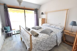 Ein Schlafzimmer mit einem Bett, zwei Nachttischen, einem Sessel, einem Kleiderschrank und einem Fenster mit Vorhängen.