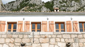 A stone building with wooden shutters and a wooden door, set against a mountainous backdrop. - Stylishly renovated stone house with comfort, sea views, pool and large garden (Grizane)