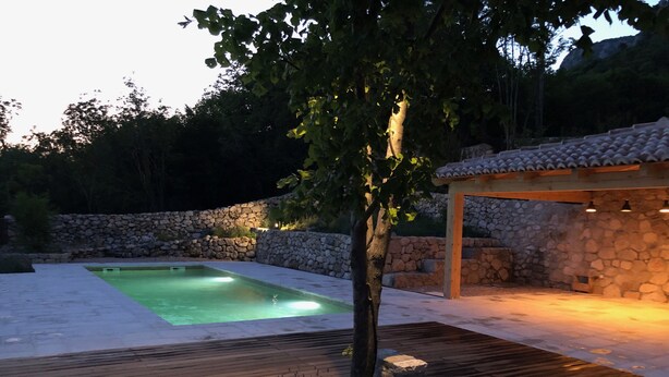A swimming pool with a wooden deck and stone walls. - Stylishly renovated stone house with comfort, sea views, pool and large garden (Grizane)
