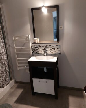 Un baño con lavamanos blanco, mueble oscuro y espejo con luz superior.