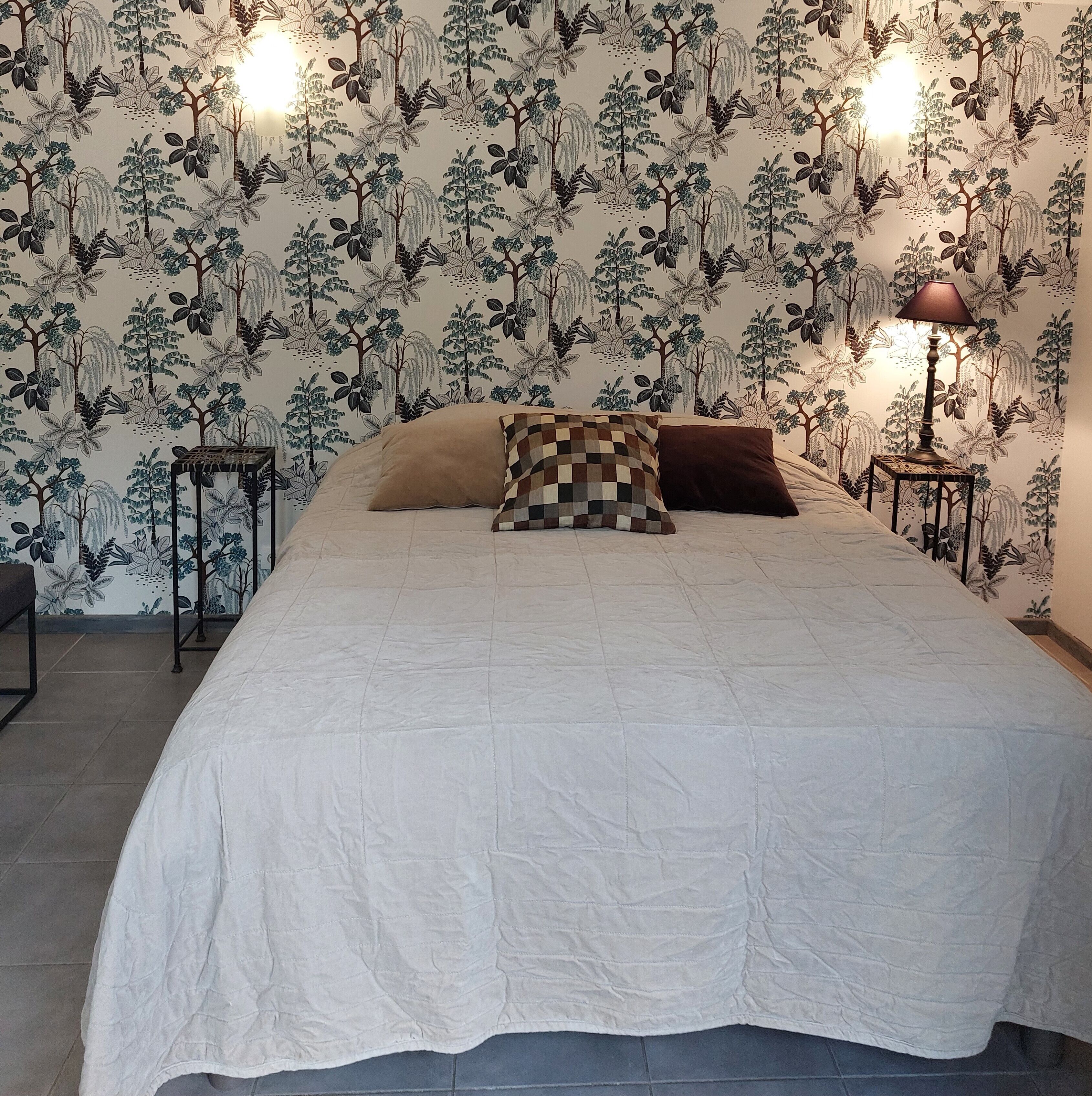 Ein Schlafzimmer mit einem großen Bett, zwei Kissen, Tapete mit Muster, einem Nachttisch mit Lampe und einem kleinen Tisch.