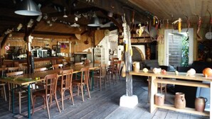 A rustic dining area with wooden tables and chairs, a bar area with stools, and hanging kitchen utensils.