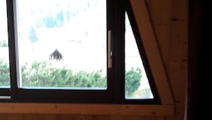 Una mesa de madera con sillas, una ventana con vista a vegetación y un techo inclinado.