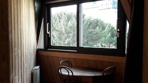 Una habitación con paredes de madera, una ventana que da a árboles, un radiador y un suelo de baldosas.