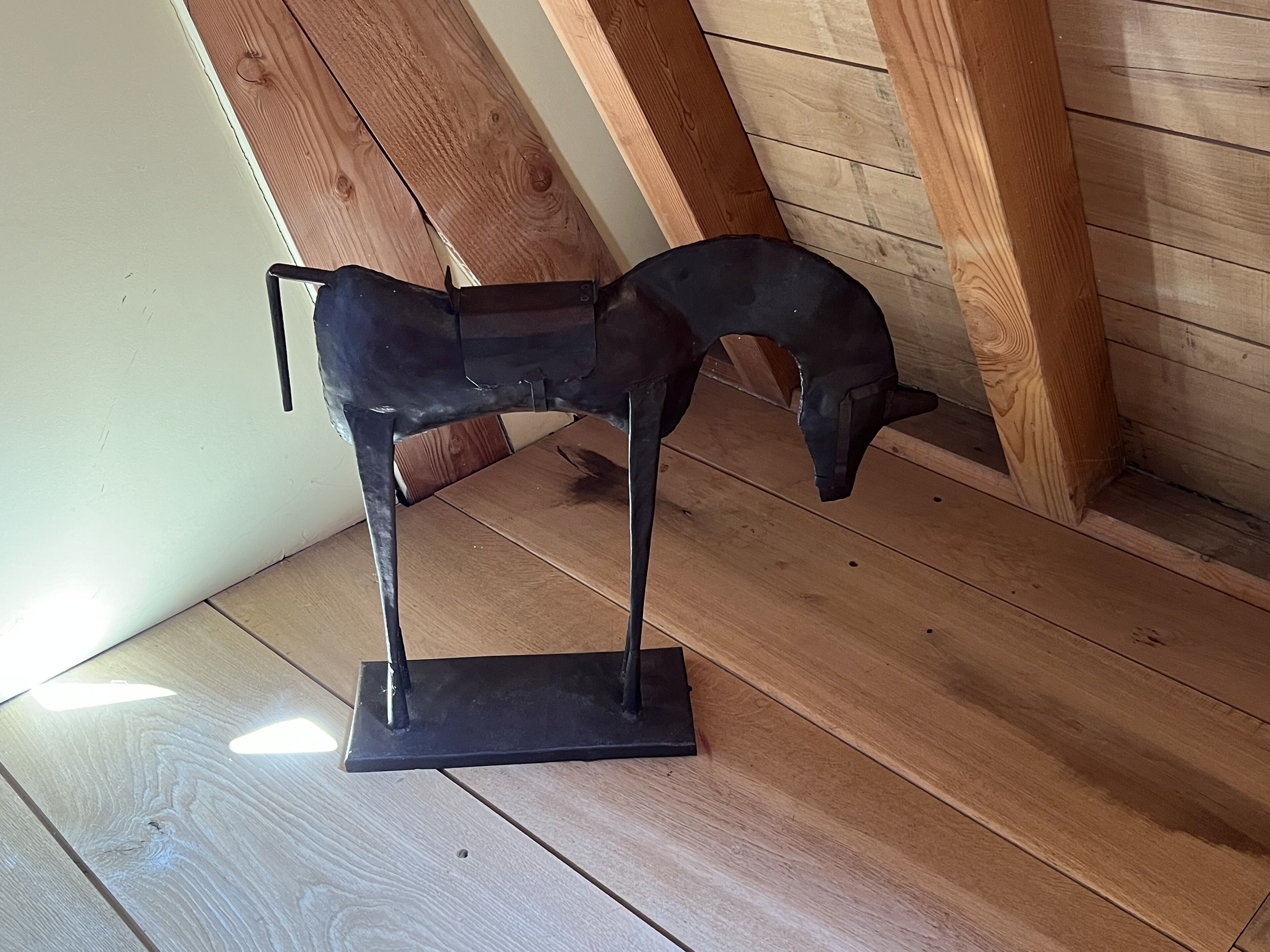A metal sculpture of a horse on a wooden floor in a room with wooden beams.