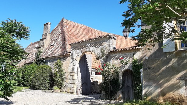 A historic stone building with a tiled roof, an arched entrance, and a gravel path leading to it.