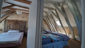 A rustic bedroom with exposed wooden beams and a sloped ceiling, featuring a bed with a striped blanket and pillows.