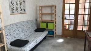 Une pièce avec un canapé aux motifs géométriques, une étagère en bois dotée de boîtes de rangement vertes et une porte en bois avec des panneaux en verre dépoli.