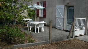 Un espace patio aménagé avec une table et des chaises, un parasol à rayures et une entrée fermée par un portail.