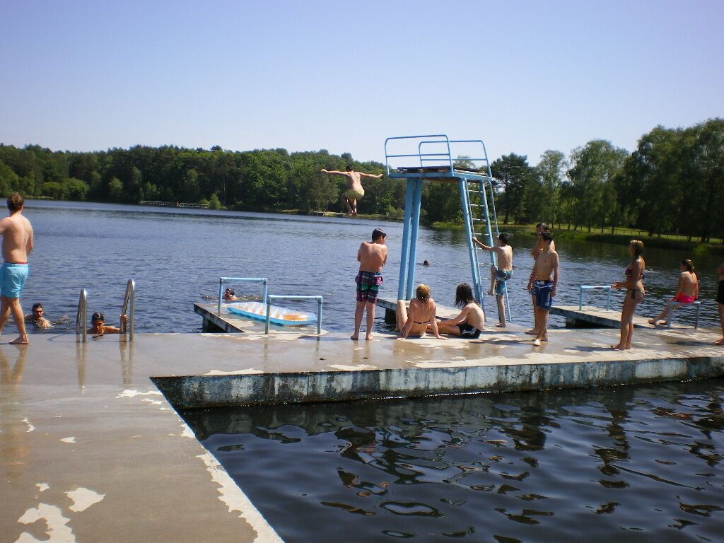 A swimming pool with a diving board, surrounded by people.