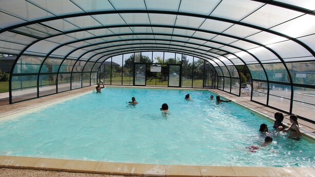 An indoor swimming pool with a curved glass roof, surrounded by a fence. - Large furnished cottage with covered terrace and parking space (Beynat)