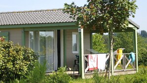 A small house with a green exterior, a tiled roof, and a porch with a table and chairs. - Large furnished cottage with covered terrace and parking space (Beynat)