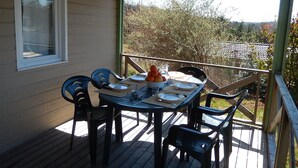 An outdoor dining area with a table and chairs, a window, and a view of trees and a fence. - Large furnished cottage with covered terrace and parking space (Beynat)