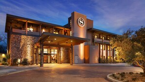 A modern hotel with a stone facade, a prominent logo, and a covered entrance.