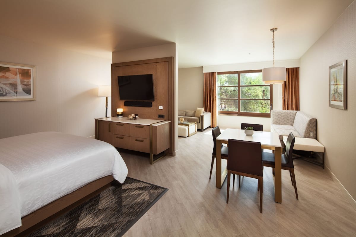 A hotel room with a bed, a desk, a chair, a TV, and a window with curtains.