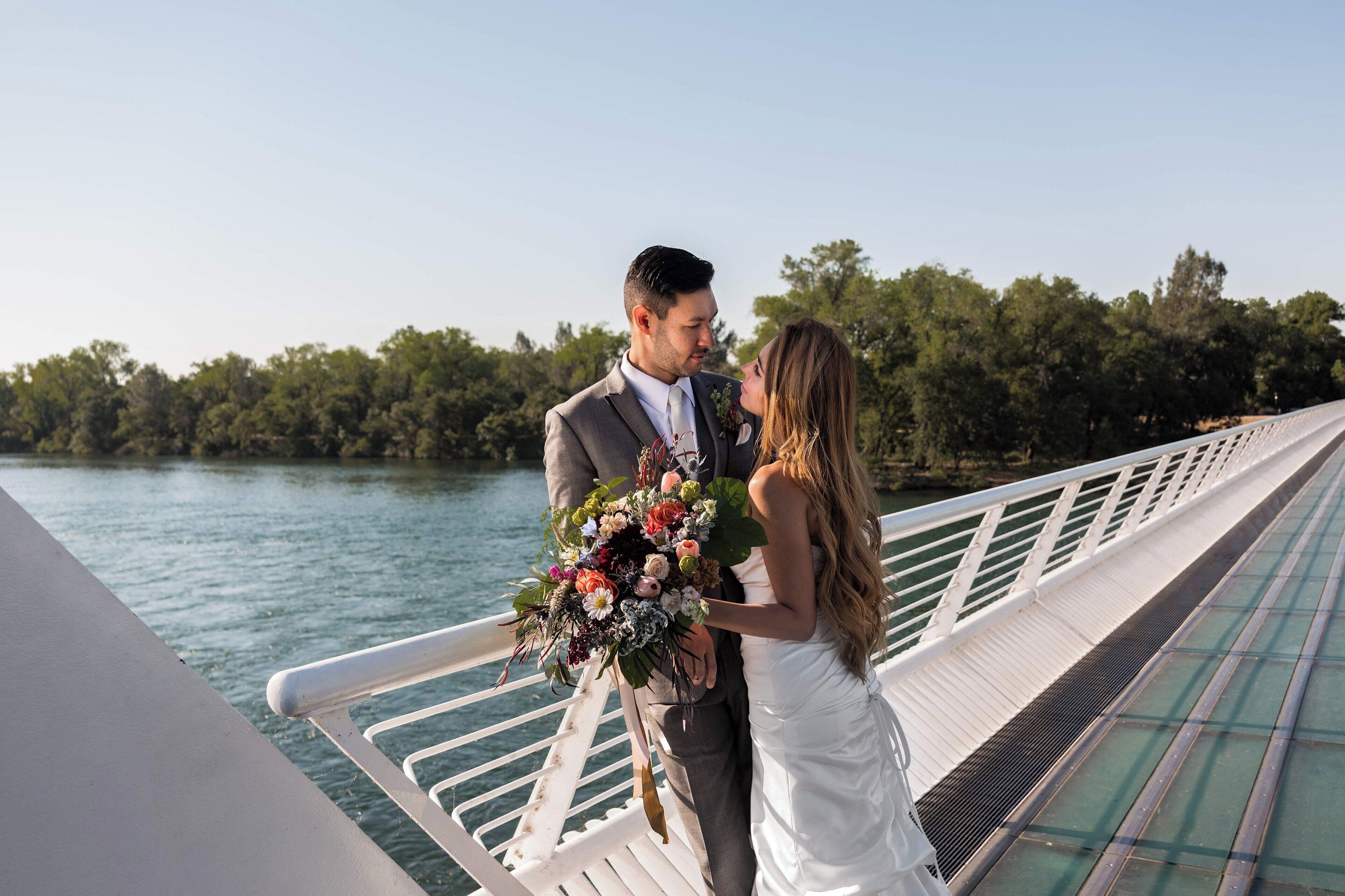 A couple on a bridge with a body of water and trees in the background.
