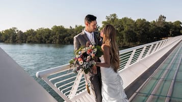 A couple on a bridge with a body of water and trees in the background.