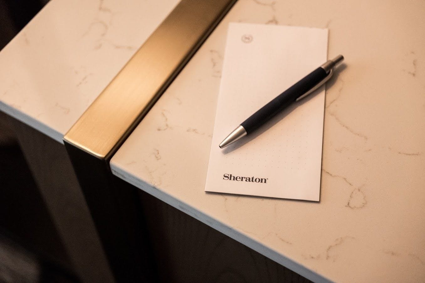 Una libreta con la palabra "Sheraton" sobre una superficie de mármol, junto a un bolígrafo.