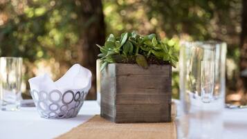 A rustic wooden planter with green foliage, a white bowl with circular patterns, and clear glassware on a table outdoors.