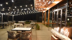 An outdoor patio area with tables and chairs, string lights, and a log fire feature.