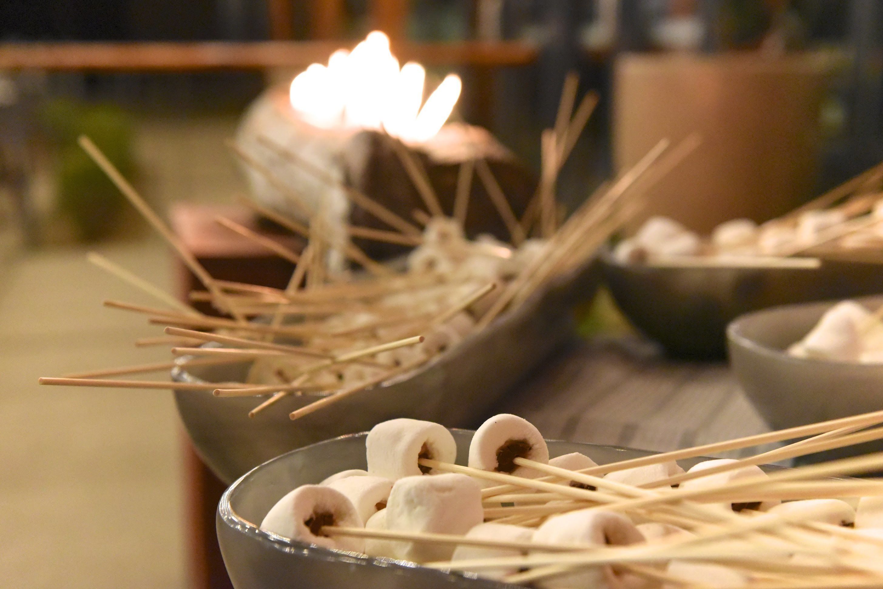 A bowl of marshmallows on sticks, a candle, and a bowl of marshmallows.