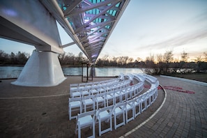 Un lieu de réception en plein air pour un mariage, avec des chaises blanches disposées en demi-cercle, une grande structure blanche et une vue sur une rivière.