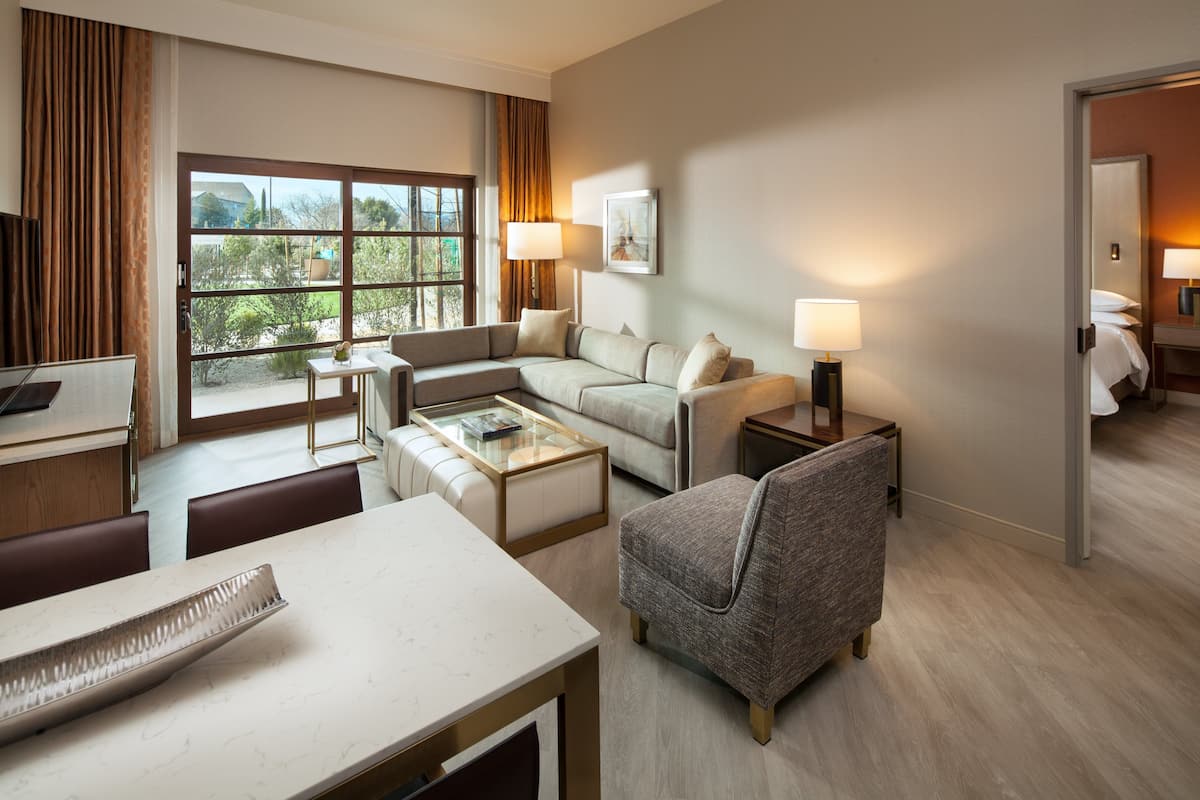 A hotel room with a sofa, armchairs, a coffee table, a desk, and a bed.