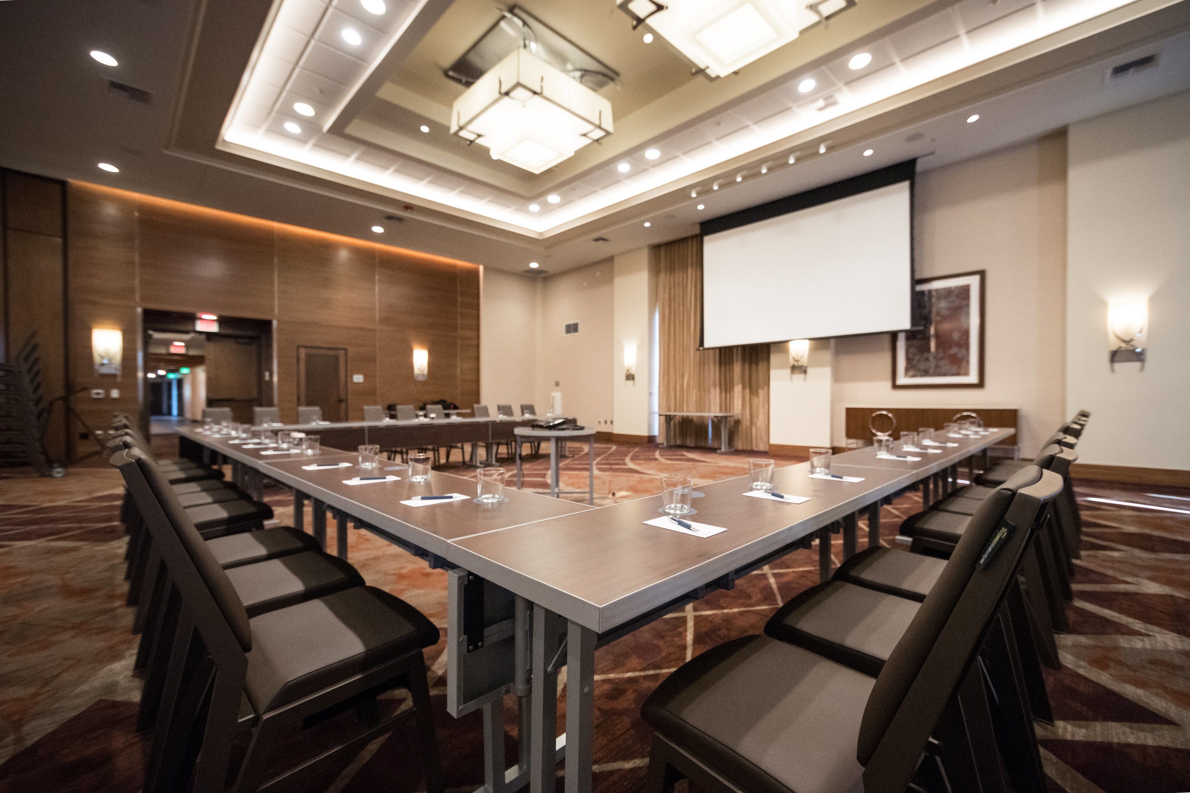 A conference room with a long table, chairs, a projector screen, and a carpeted floor.