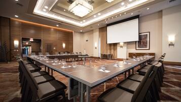 A conference room with a long table, chairs, a projector screen, and a carpeted floor.