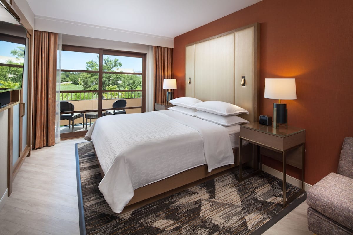 A hotel room with a large bed, two bedside lamps, a desk, and a view of the outdoors.