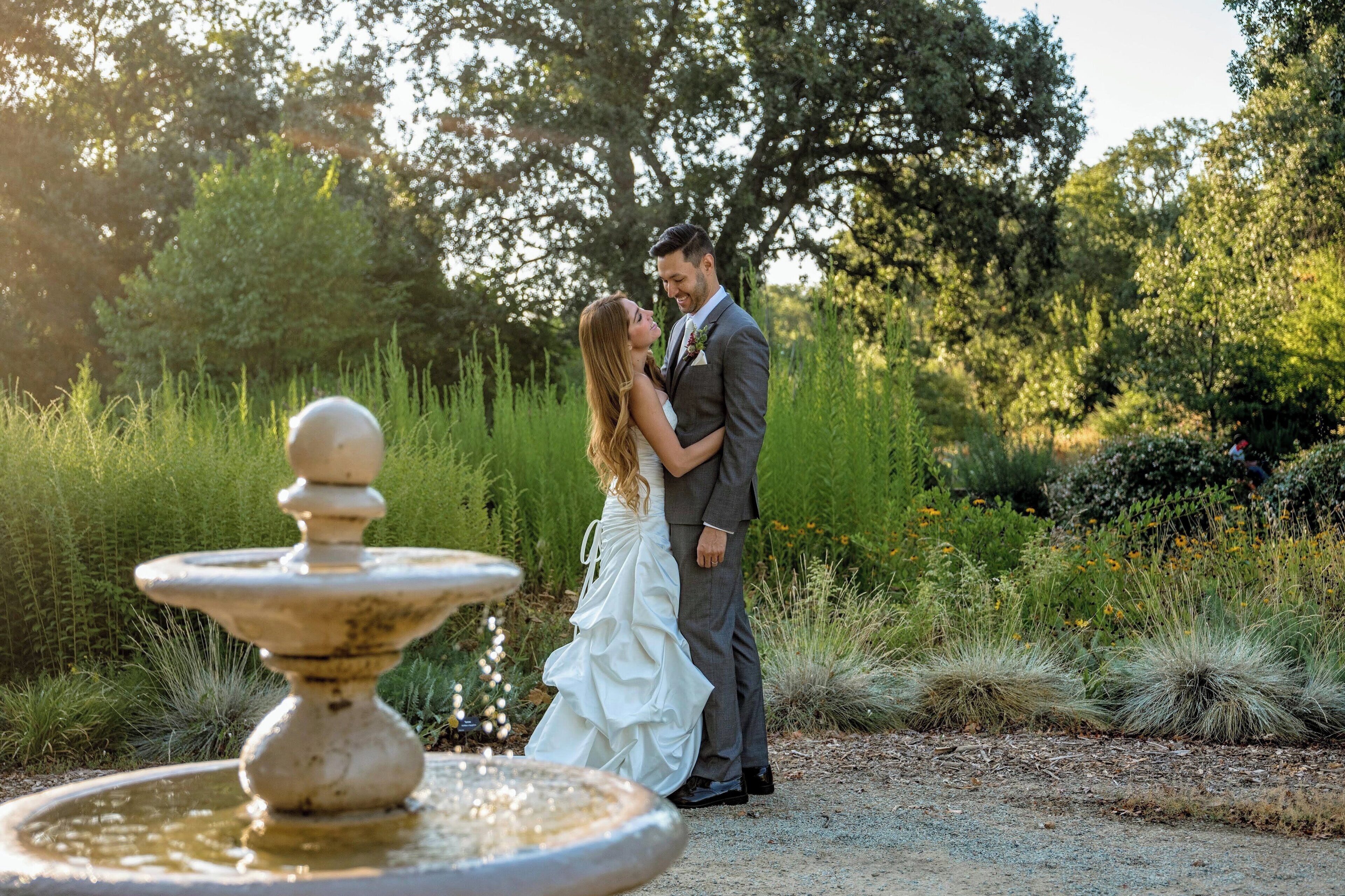 A couple embracing near a fountain in a garden setting.