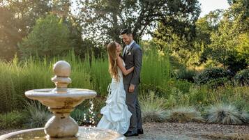 A couple embracing near a fountain in a garden setting.
