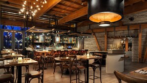 A restaurant with wooden interiors, bar area, and tables with chairs.