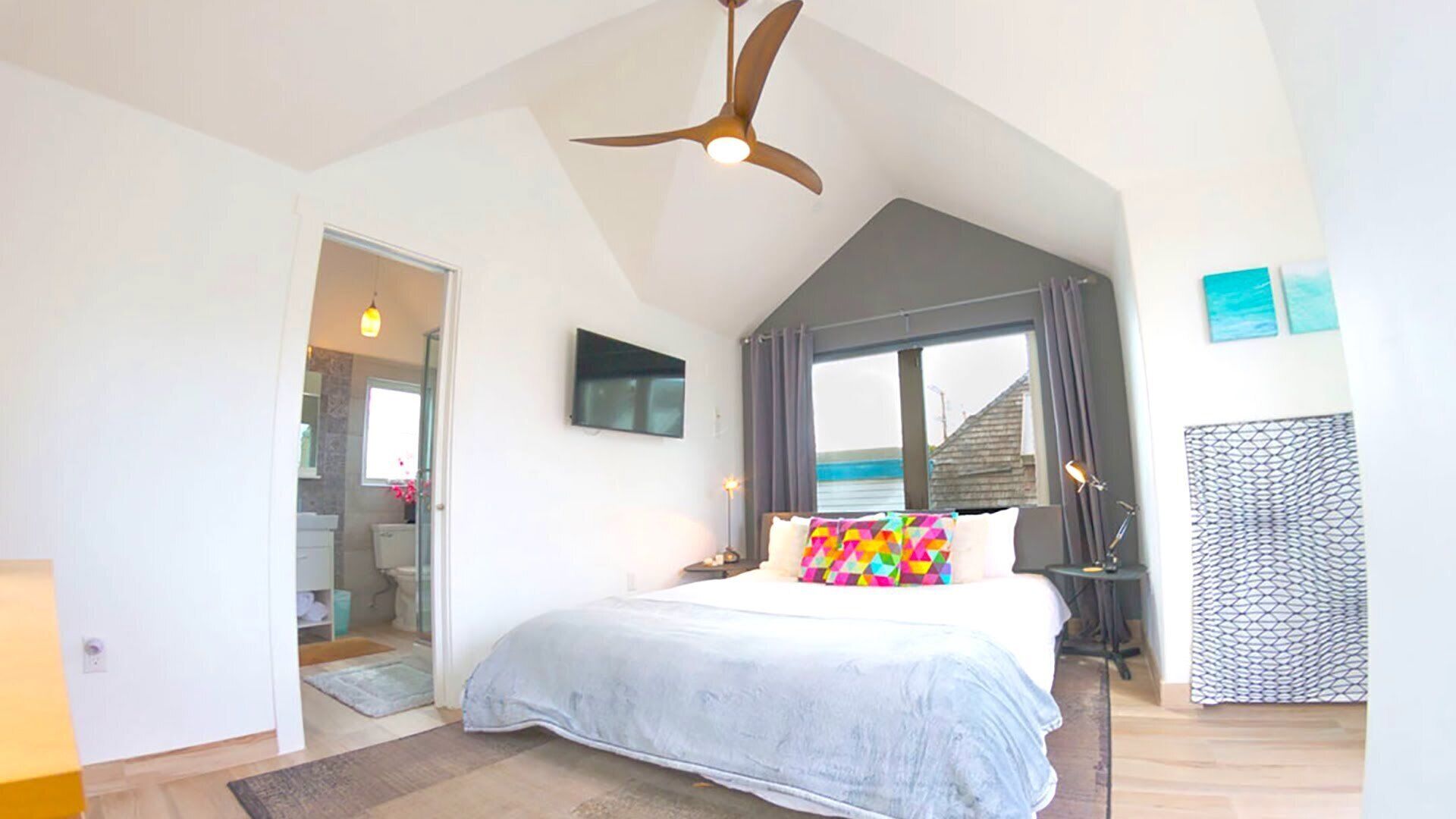 A bedroom with a bed, a ceiling fan, a TV, and a window with curtains.