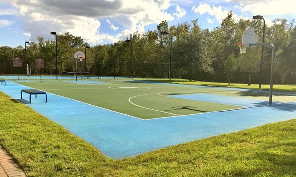 An outdoor basketball court with a blue surface, surrounded by trees and a fence.